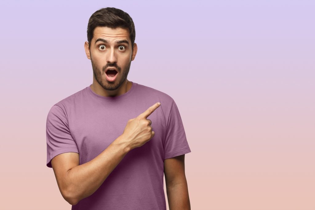Young surprised man in purple t-shirt pointing right with his finger, shouting WOW